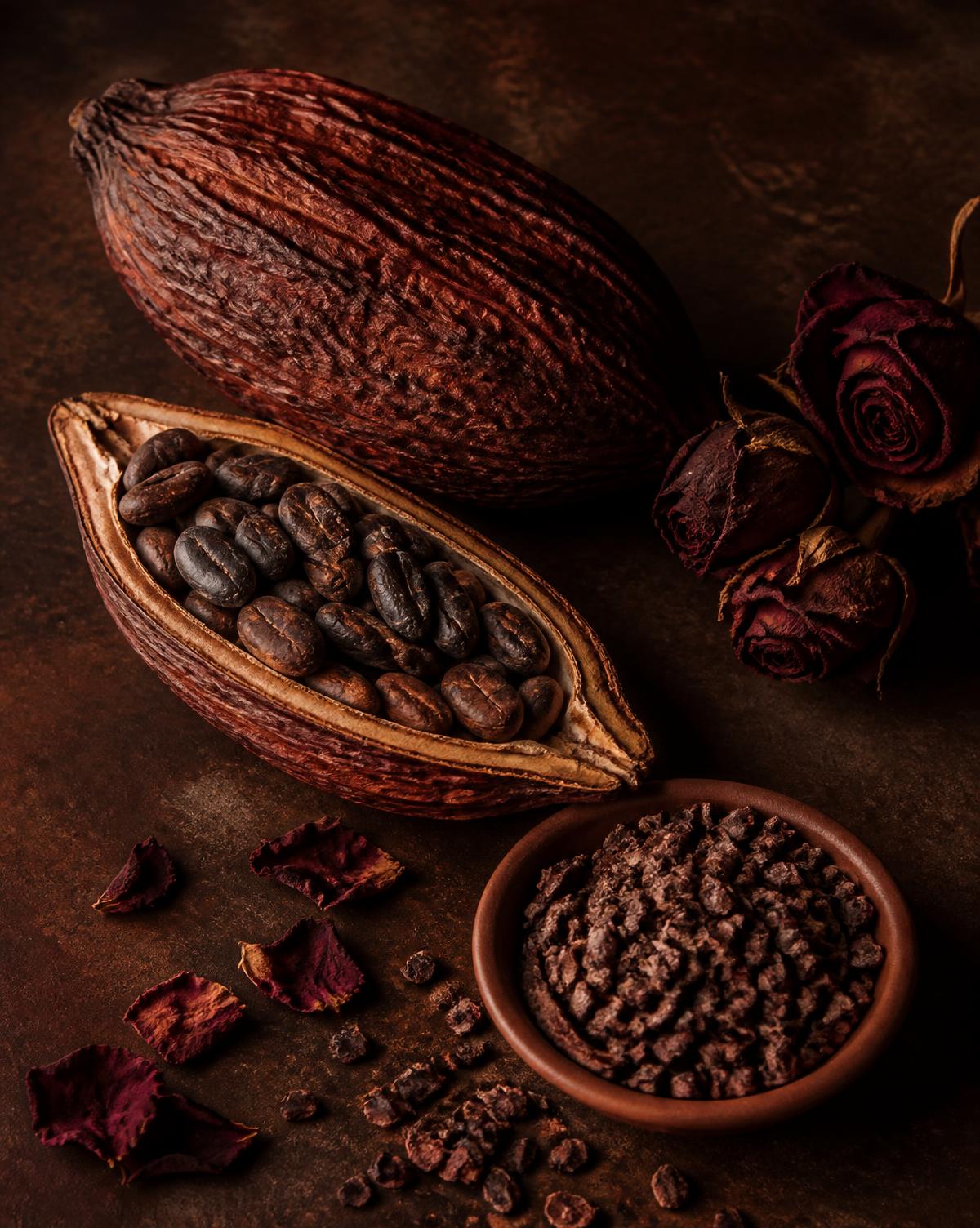 Cacau, nibs e rosas secas sobre pedra escura